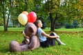 Sad girl with big teddy bear and balloons in the park. Problems teenagers at school