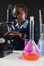 Schoolgirl using microscope against black background Royalty Free Stock Photo