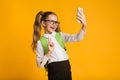 Schoolgirl Using Smartphone Taking Selfie Gesturing V-Sign, Yellow Background Royalty Free Stock Photo