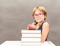 Schoolgirl wearing glasses sitting at a table with a stack of th