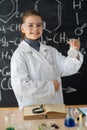 schoolgirl in white coat doing experiments with liquids in chemistry lab, school blackboard background with hand drawn Royalty Free Stock Photo