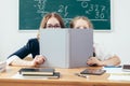 Schoolgirls hiding behind book sitting in a classroom