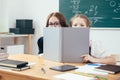 Schoolgirls hiding behind book sitting in a classroom