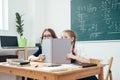 Schoolgirls hiding behind book sitting in a classroom