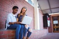 Schoolgirls sitting against brick wall and using laptop