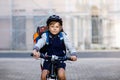 Schoolkid boy in safety helmet riding with bike in the city with backpack. Happy child in colorful clothes biking on