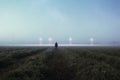A science fiction concept. A man standing in a field back to camera looking into the sky, with glowing UFO orbs on the horizon