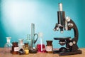 Science. Old vintage microscope and laboratory glass bottles on table front gradient mint blue background. Retro