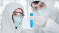 Scientific background of biological reseach scientists in biohazard protection clothing experimenting and holding test tube on