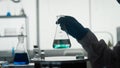 Scientific experiment. A flask with a clear liquid and a green reagent in a man's hand close up. Royalty Free Stock Photo