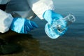 Scientist in chemical protective suit with conical flask taking sample from river for analysis, closeup Royalty Free Stock Photo