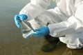 Scientist in chemical protective suit with conical flask taking sample from river for analysis, closeup Royalty Free Stock Photo