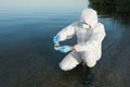Scientist in chemical protective suit with conical flask taking sample from river for analysis Royalty Free Stock Photo