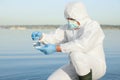 Scientist in chemical protective suit with conical flask taking sample from river for analysis Royalty Free Stock Photo