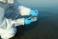 Scientist in chemical protective suit with florence flask taking sample from river for analysis, closeup Royalty Free Stock Photo