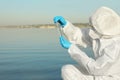 Scientist in chemical protective suit with test tube taking sample from river for analysis Royalty Free Stock Photo