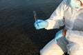 Scientist in chemical protective suit with test tube taking sample from river for analysis, closeup Royalty Free Stock Photo