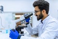 Scientist conducts experiments, adjusts specimen in petri dish and looking on it into microscope Royalty Free Stock Photo