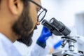 Scientist conducts experiments, adjusts specimen in petri dish and looking on it into microscope Royalty Free Stock Photo