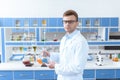 Scientist in eyeglasses holding flask with reagent and looking at camera