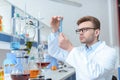 Scientist in eyeglasses and white coat examining test tube in laboratory