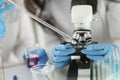 Scientist in gloves conducts laboratory studies of liquid on microscope