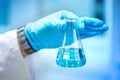 Scientist hand holding glass with blue liquid, making experiments and carrying out probes