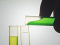 Scientist hand pouring a green chemical solution from a laboratory glass test tube into a scientific cylinder with yellow liquid f Royalty Free Stock Photo