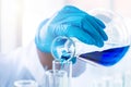 Scientist hand with rubber glove pouring blue chemical liquid from glass flask to test tube. Royalty Free Stock Photo