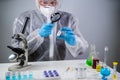 Scientist in hazmat suit and goggles holding vaccine bottle and magnifying glass, looking and research. Epidemiology virus test.