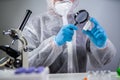 Scientist in hazmat suit and goggles holding vaccine bottle and magnifying glass, looking and research. Epidemiology virus test. Royalty Free Stock Photo