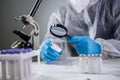 Scientist in hazmat suit and goggles holding vaccine bottle and magnifying glass, looking and research. Epidemiology virus test. Royalty Free Stock Photo