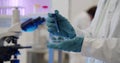 Scientist holding and analyzing blue liquid in petri dish in laboratory.