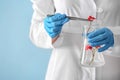 Scientist holding tweezers and flask with flowers on color background