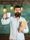 Scientist holds book and drinks coffee, chalkboard on background, copy space. Coffee break concept. Man with beard on Royalty Free Stock Photo