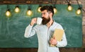 Scientist holds book and drinks coffee, chalkboard on background, copy space. Man with beard on calm face in classroom Royalty Free Stock Photo