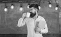 Scientist holds book and drinks coffee, chalkboard on background, copy space. Man with beard on calm face in classroom Royalty Free Stock Photo