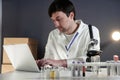 Scientist in lab coat and eyeglasses working at workplace with laptop in laboratory. Male doctor researcher are doing Royalty Free Stock Photo