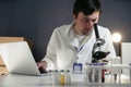 Scientist in lab coat and eyeglasses working at workplace with laptop in laboratory. Male doctor researcher are doing Royalty Free Stock Photo