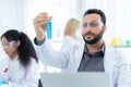 Scientist in lab coat and safety glasses holding test tube with blue solution at modern laboratory. Look at tube and analysis. Royalty Free Stock Photo