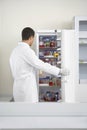 Scientist Looking At Specimen Bottles In Refrigerator At Laboratory