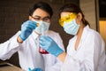 Scientist man and woman wear white coat and blue gloves holding dropper and drop red water to tube science.