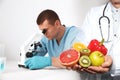 Scientist with microscope at table and his colleague. Food quality analysis Royalty Free Stock Photo