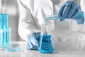 Scientist pouring light blue liquid from test tube into flask in laboratory, closeup Royalty Free Stock Photo