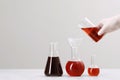 Scientist pouring liquid from beaker into round bottom flask on white table against light background, closeup. Space for text Royalty Free Stock Photo