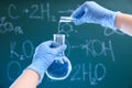 Scientist pouring liquid into flask against chalkboard. Chemistry glassware Royalty Free Stock Photo