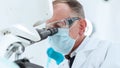 scientist in a protective mask looking through a microscope.