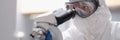 Scientist in a protective suit looking through a microscope in modern equipped laboratory