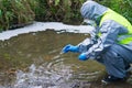 Scientist in a protective suit and mask, releases into the pond bio plants for reproduction from a Petri dish