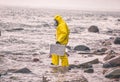 Scientist in protective suit with silver case walking on rocky beach